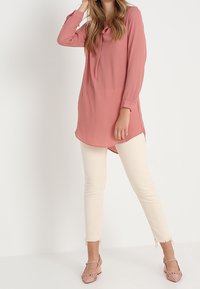 Långärmad rosa blus med knäppt krage, kombinerad med krämfärgade skinny jeans och ljusrosa skor med ett strukturerat mönster.