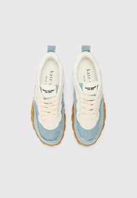 Des baskets bleu clair et crème présentent un dessus en denim et en textile pelucheux, des lacets crème et une semelle en caoutchouc texturé. Logo emblématique visible sur la languette.