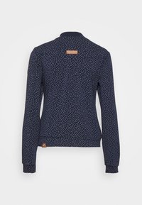 Marinblå långärmad skjorta med vita polka prickar, rund krage och elastiska ärmslut. Har en tygetikett på baksidan. Slät textur.