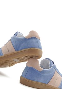 Hellblaues Wildleder-Sneaker mit beige Akzenten, runder Form, strukturierten Gummisohlen und einfachem Schnürdesign. Markenname auf der Seite sichtbar.