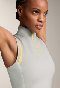 Grey athletic top with a high collar and yellow zipper detail. Smooth texture with fitted design, showcasing the shoulders and arms.