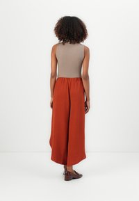 Tan ribbed tank top paired with rust wide-leg trousers. Loose fit with an elastic waistband and natural fabric texture. Brown shoes visible.