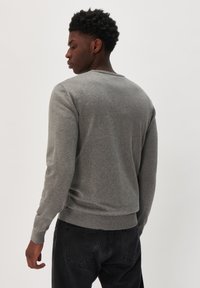 Suéter de punto gris con cuello redondo y puños acanalados. Textura suave y diseño ajustado. Se lleva con jeans de mezclilla negros.