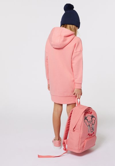 Vestito rosa con cappuccio, dal taglio morbido, abbinato a uno zaino rosa con una grafica di un elefante. Sneakers bianche completano il look.
