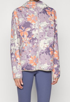 Veste à capuche violet clair avec imprimé floral blanc et orange portée avec des leggings bleus, vue de face du cou aux hanches.