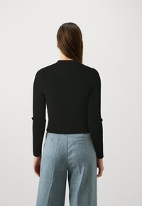 A blusa preta de manga longa com textura ribada apresenta uma silhueta ajustada e um decote redondo, combinada com calças largas de tom azul claro.