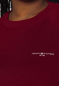 Bordeaux geribbelde sweatshirt met een ronde hals, voorzien van een klein wit "TOMMY HILFIGER" logo en de tekst "EST. 1985" op de borst.