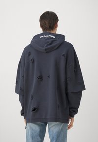 Felpa oversized blu navy con un motivo floreale testurizzato, dotata di cappuccio con cordino e polsini a costine. Logo sul retro: "les benjamins."