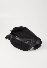 Schwarze Stoffgürteltasche mit einem Reißverschluss-Hauptfach, Innenfach und elastischen Schnüren auf der Vorderseite. Strukturierter Material mit glatter Oberfläche.