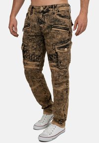 Pantaloni cargo in una tonalità marrone sbiadito con accenti neri, caratterizzati da tasche con zip e un design testurizzato. Realizzati in un resistente tessuto di denim.