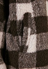 Pledas flisinė medžiaga, kurioje dominuoja tamsiai ruda, šviesiai ruda ir kreminė spalvos; minkštas, tekstūruotas paviršius su jaukia, pūsta išvaizda.