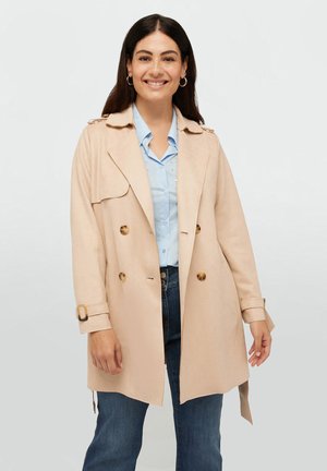Cappotto beige con design doppiopetto, bottoni dorati e una cintura. Indossato sopra una camicia azzurra, abbinato a jeans blu scuro.