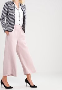 Blazer rayé noir et blanc, chemise blanche à boutons, pantalon large rose pâle, et escarpins noirs. Tissu lisse avec coupe décontractée.
