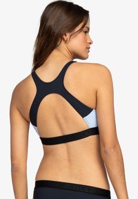Blå och marinblå sport-bh med racerback-design. Har ett svart, märkesband och mjukt, stretchigt tyg. Accenter med kontrasterande färg.