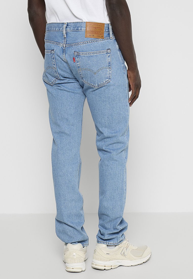 Jeans de mezclilla azul claro con corte recto, que cuentan con dos bolsillos traseros, una etiqueta de cuero marrón y sutiles detalles de costura.