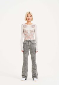 Top a maniche lunghe in rete con un design grafico colorato; jeans grigi a zampa d'elefante con motivi intricati; sneaker bianche completano il look.