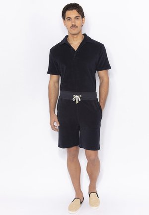 Polo pour homme bleu marine à manches courtes en tissu doux, avec un col, une patte de boutonnage, et un short coordonné avec un cordon de serrage réglable.