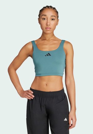 Teal sportski crop top s uskim naramenicama i crnim logotipom u sredini, uparen s crnim treniračkim hlačama s elastičnim strukom, glatka tekstura tkanine.