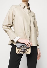 Pieni käsilaukku, jossa on teksturoitu beige ja musta käärmepuolikuviollinen pinta, yläluukku, hopeiset metalliosat ja ketjuhihna olalle.