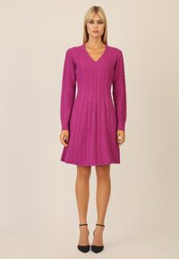 Fuchsia gestricktes Kleid mit V-Ausschnitt, ausgestattet mit Kabelstrick-Textur, langen Ärmeln und einem schwingenden Rock, ergänzt durch schwarze High Heels.