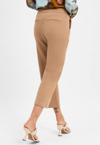 Beige cropped trousers with a smooth texture, two back pockets, worn with light-colored heels featuring a twist design.