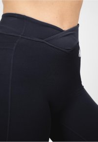 Zwarte high-waisted legging met een gladde stof, kruisbandontwerp en gestikte naden voor een fitted look.