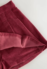 Shorts bordeaux dintr-un material moale și texturat, având o pliere la tiv și un centură netedă cu detalii de cusătură îngrijită.