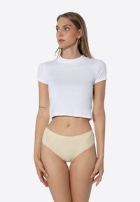 T-shirt blanc court à manches courtes associé à une lingerie taille haute beige clair. Texture lisse, design simple et silhouette ajustée.