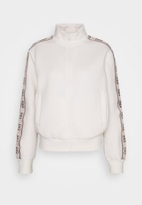 Veste blanche zippée avec col haut, rayures beiges à motif logo sur les manches, et deux poches avant.