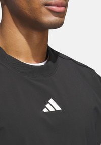 Černá sportovní mikina s kulatým výstřihem, na horní levé straně s bílým trojúhelníkovým logem. Hladká textura, minimalistický design.