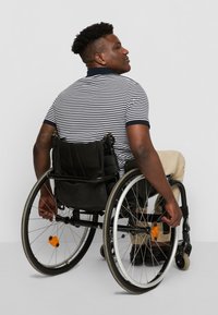 Black wheelchair with aluminum frame, black seating, and a rear bag. Person in a striped polo shirt and khaki pants, adjusting wheel.