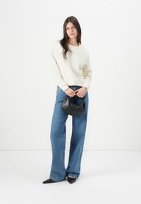 Light yellow sweatshirt with a round neckline, paired with blue wide-leg denim jeans. Holding a small black handbag with a rounded shape.