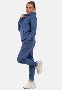 Blauwe fleece hoodie met kangoeroezak, gecombineerd met bijpassende joggerbroek. Aangevuld met elastische manchetten en chunky witte sneakers.