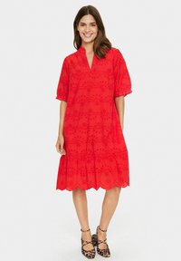 Red, short-sleeved dress with a scalloped hem, floral embroidery, and a v-neck. Worn with leopard print ankle strap shoes.