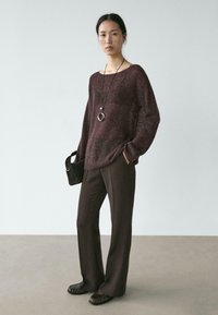 Bordeaux gebreide trui met brede halslijn, gecombineerd met bruine recht gesneden broek. Accessoires zijn onder meer een lange ketting en een zwarte tas met textuur.