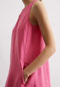 Rosa Leinenärmeloses Kleid mit hohem Ausschnitt, seitlichen Taschen und lässiger Passform. Die Textur ist leicht zerknittert mit einem weichen Finish.
