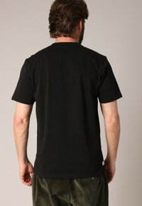 T-shirt noir à manches courtes en coton avec un col rond. Texture lisse, design uni et une étiquette visible au bas de l'ourlet.