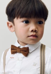White shirt with small embroidered vehicles, paired with a brown corduroy bow tie and beige suspenders featuring thin stripes.
