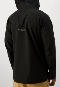 Crna vodootporna jakna s kapuljačom, sadrži Columbia Titanium logo i glatku mat teksturu, dizajnirana za vanjsku upotrebu.