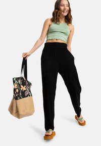 Pantaloni neri a gamba larga, top corto a coste verde chiaro, borsa a fiori con base beige e sandali platform marroni con dettagli verdi.