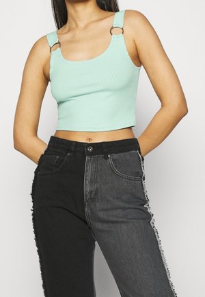 Muntgroen geribd crop top met zilveren ringen aan de bandjes, gecombineerd met zwart-grijze gesplitste spijkerbroek met rafelige zijkanten.