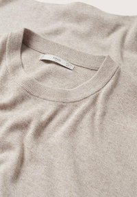 Pull à manches courtes en tricot côtelé beige avec un col rond, présentant une texture douce et une étiquette de marque visible à l'intérieur du col.