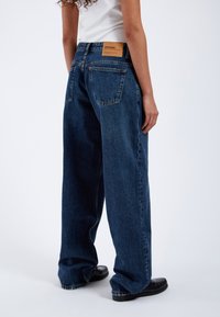 Baggy mörkblå denimjeans med en ljusbrun läderlapp på baksidan av linningen. Har klassiska bakfickor och en rak ben design.