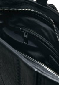 Interno della borsa nera che mostra un rivestimento in tessuto liscio e una piccola tasca con zip dotata di un tirante in metallo.