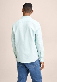 Chemise boutonnée vert menthe clair avec manches longues, ourlet droit et texture douce, portée avec un jean en denim bleu.