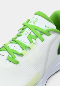 Λευκό αθλητικό παπούτσι με πράσινες λεπτομέρειες, υφασμένο επάνω μέρος, εμφανές σύστημα κορδονιού, οπές για αερισμό και μαύρη λεπτομέρεια λογότυπου.