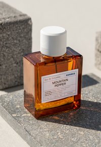 Kwadratowa butelka z bursztynowego szkła z białą nakrętką; etykieta głosi "PIPER MOUNTAIN", 50 ml. Kreda o fakturze szarego kamienia w tle.