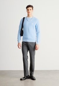 Világoskék bordázott pulóver kis logóval, sötétszürke, szabott nadrággal és fekete cipővel párosítva, kiegészítve fekete táskával és ezüst lánccal.