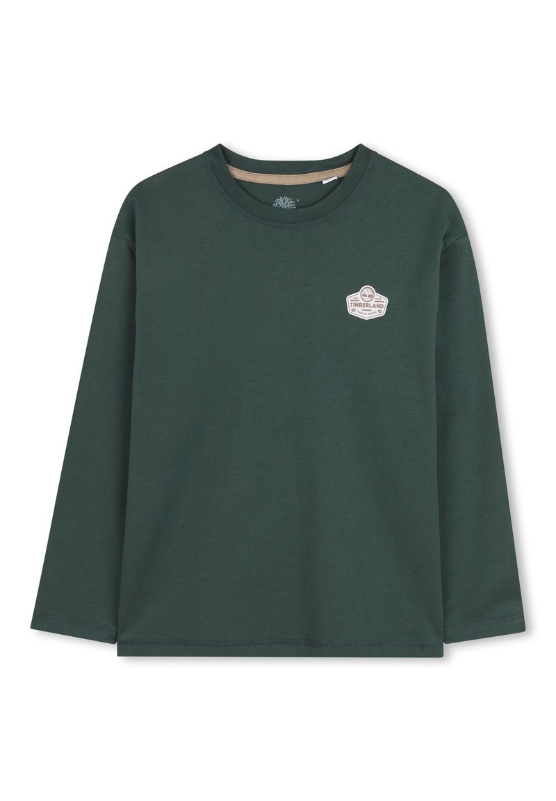 Chemise à manches longues en coton vert foncé avec un col rond et un petit patch logo blanc sur la poitrine gauche. Texture lisse.