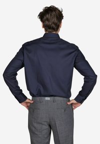 Dunkelblaues Poloshirt aus glattem Stoff, kombiniert mit grauen karierten Hosen mit Gesäßtaschen und Reißverschlüssen.